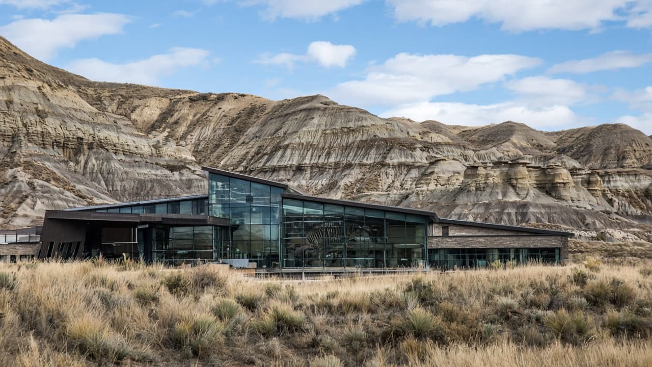 A glass museum in the Drumheller badlands, a dinosaur skeleton visible through the windows
