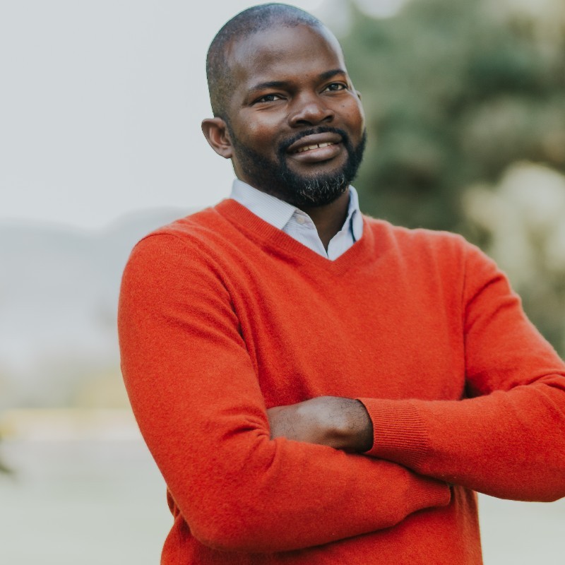 Peter Akarakiri, arms crossed, wearing an orange sweater outdoors.